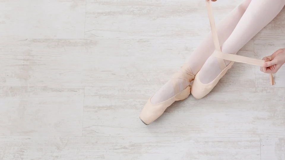 Ballet dancer tying pointe shoes on wooden floor