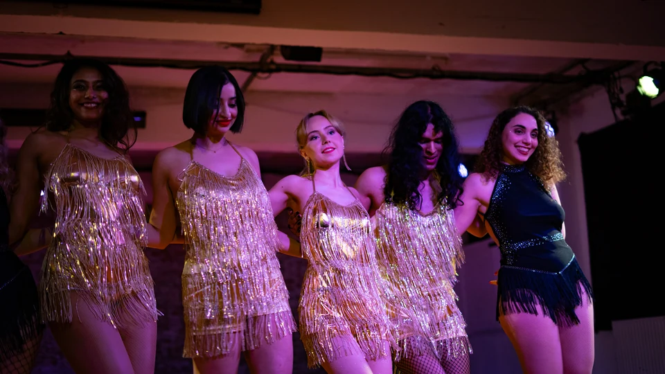 Five dancers in golden fringe costumes on stage