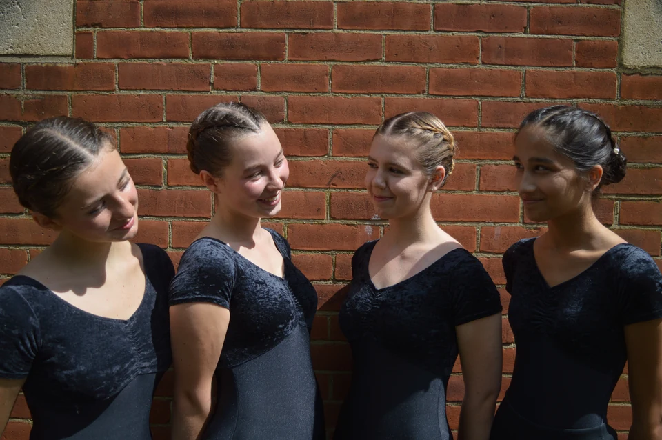 Four ballet dancers in black outfits posing together
