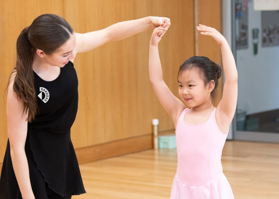 Dance instructor guiding young girl in ballet class