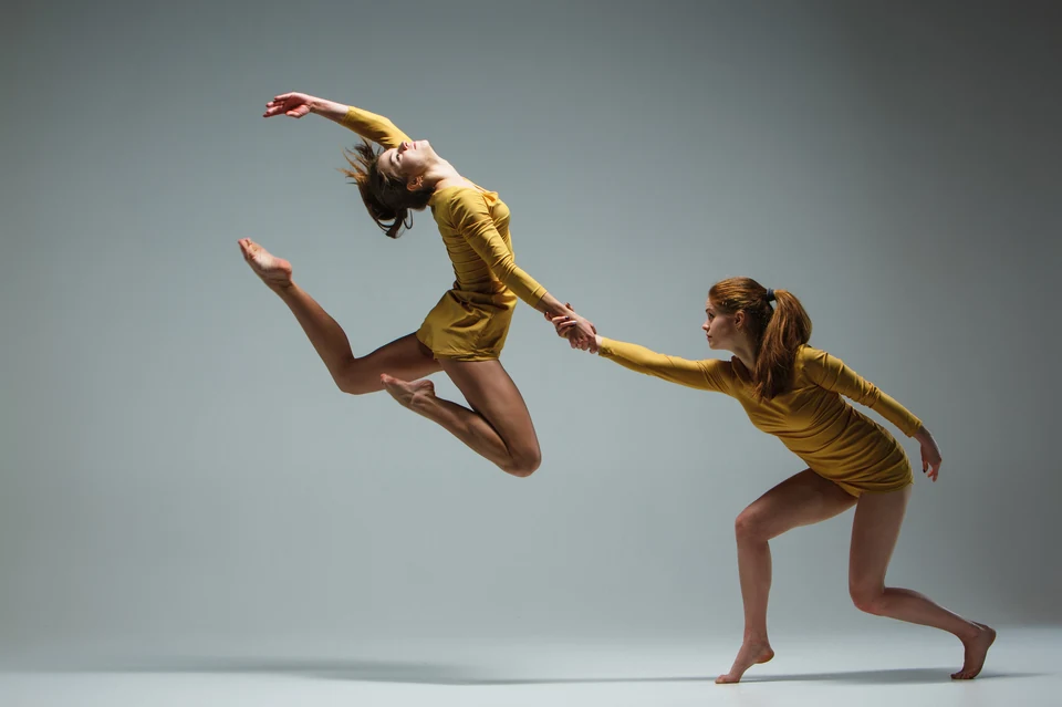 Two dancers in yellow dresses performing a leap