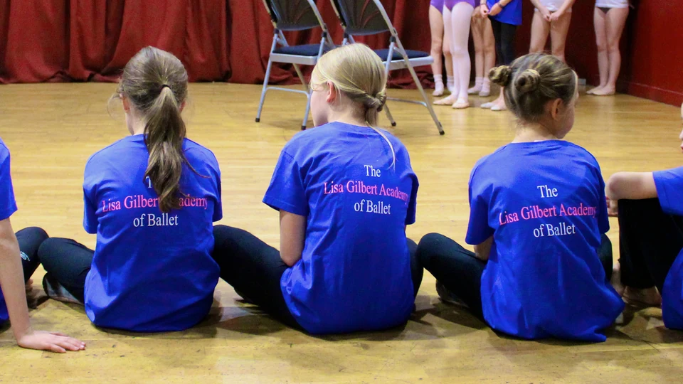 Children in blue shirts sitting on the floor
