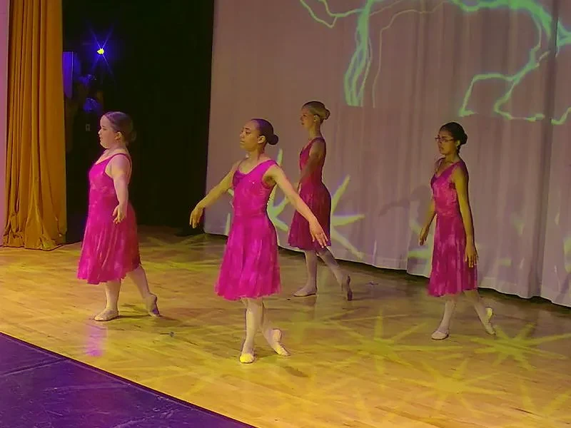 Four young dancers in pink dresses performing on stage