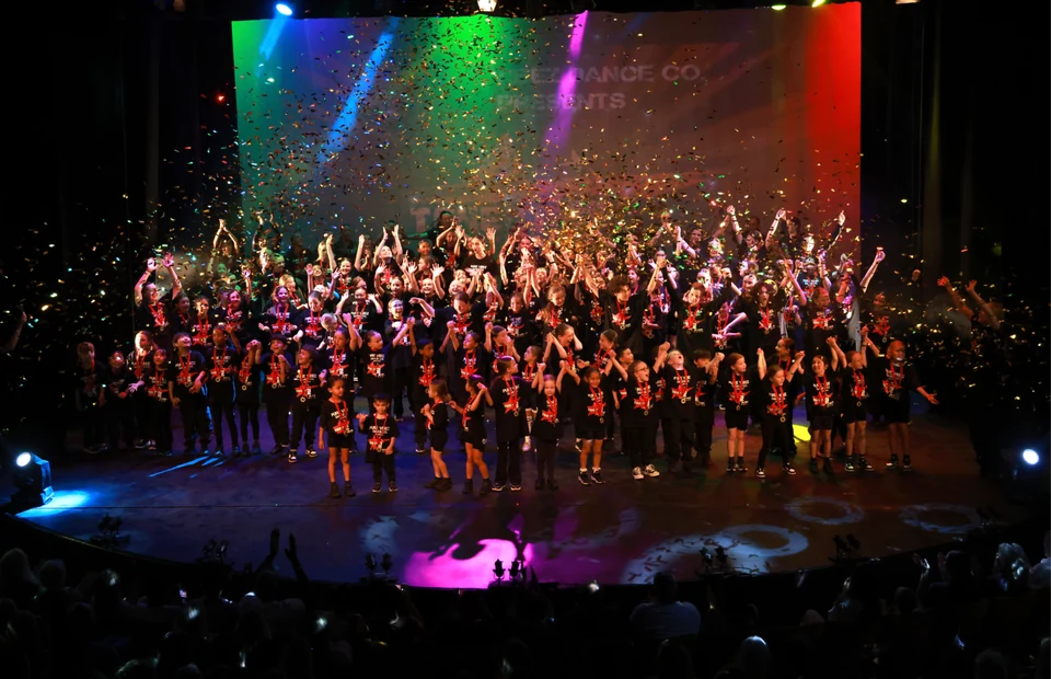 Large group of dancers performing on stage with confetti