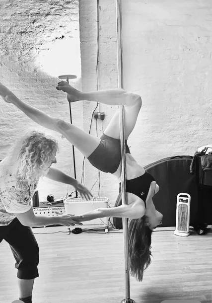 Pole dancer performing with instructor assistance