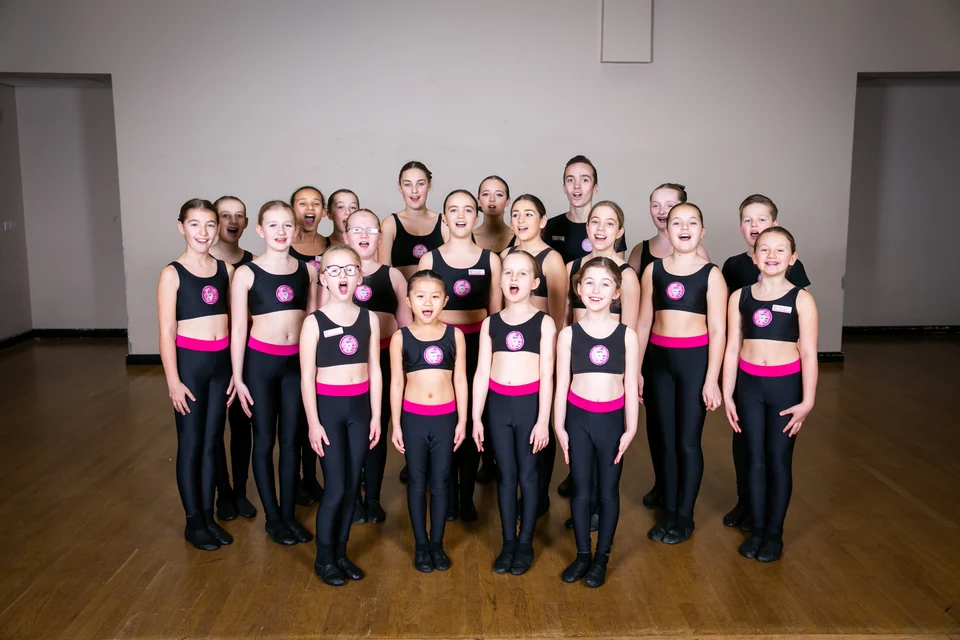 Group of young dancers in black outfits with pink accents